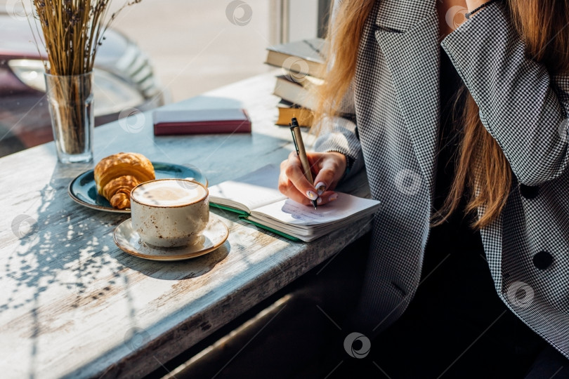 Скачать Молодая женщина сидит за столом у окна и что-то пишет в блокноте. фотосток Ozero