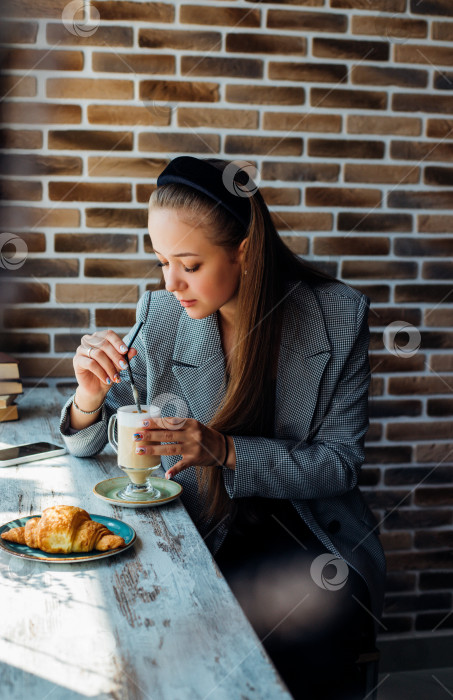 Скачать Молодая женщина сидит за столиком у окна в кафе и пьет кофе. фотосток Ozero