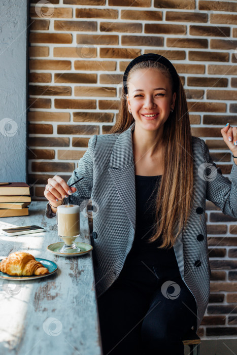 Скачать Молодая женщина сидит за столиком у окна в кафе и пьет кофе. фотосток Ozero