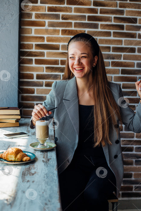 Скачать Молодая женщина сидит за столиком у окна в кафе и пьет кофе. фотосток Ozero