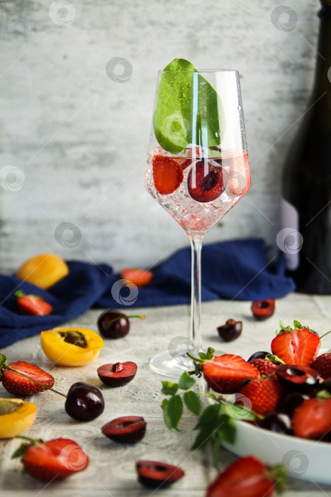 Скачать Искрящееся вино с ягодами. Освежающий охлаждающий игристый летний напиток со свежей клубникой, вишней и кубиками льда. Шампанское просекко с кубиками льда и ягодами фотосток Ozero