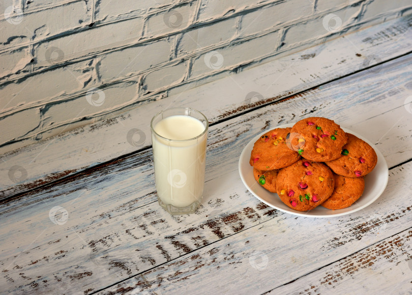 Скачать Тарелка с горкой свежего овсяного печенья в разноцветной глазури и стаканом горячего молока на столе из светлого дерева. фотосток Ozero