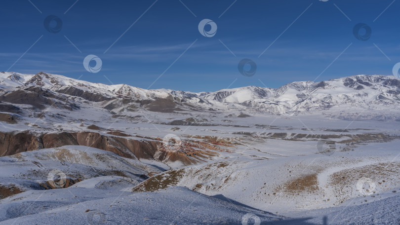 Скачать Заснеженный горный хребет с красно-коричневыми склонами на фоне голубого неба. фотосток Ozero
