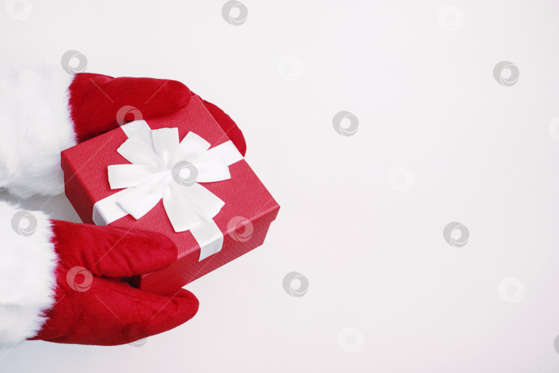 Скачать Санта в красных перчатках дарит подарок. Красная коробка с бантом в руках Санта-Клауса, выделенная на белом фоне. Концепция Рождества и Нового года. Пространство для копирования фотосток Ozero