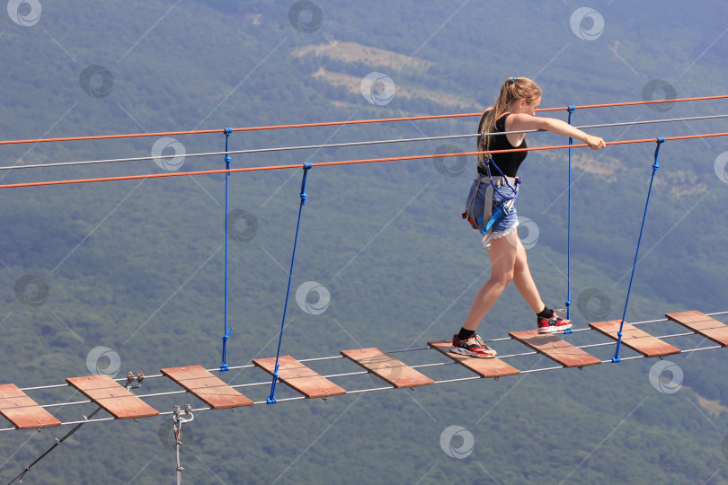 Скачать Девушка идет по подвесному мосту между скалами в горах. фотосток Ozero