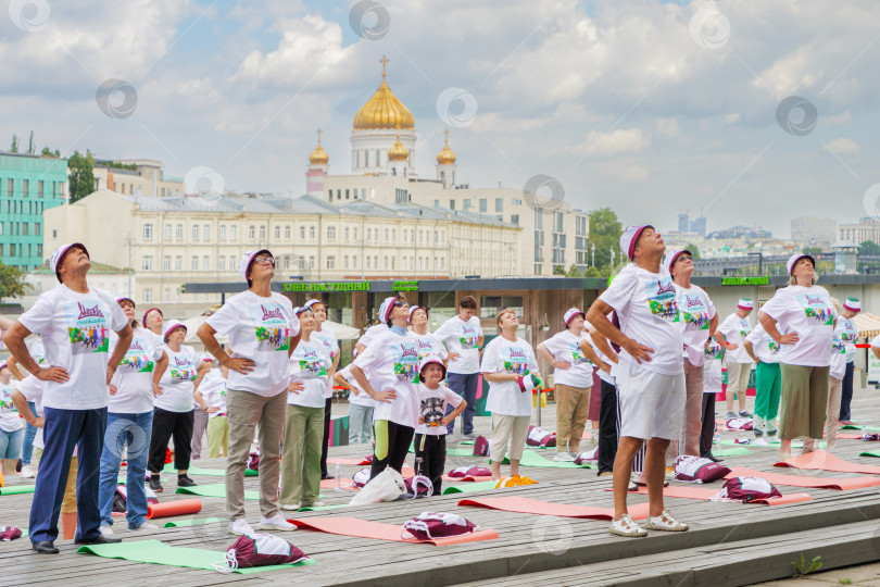 Скачать Московские пенсионеры делают гимнастику в парке Музеон на фоне храма Христа Спасителя, голубого неба и красивых кучевых облаков. Все одеты в фирменные московские футболки и головные уборы, подаренные правительством Москвы. фотосток Ozero