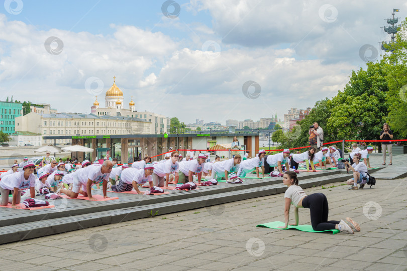 Скачать Пенсионеры, участники спортивного праздника программы "Московское долголетие", в фирменных московских футболках и шапочках, стоя на разноцветных гимнастических ковриках, выполняют гимнастику под руководством опытного тренера в парке Музеон на фо... фотосток Ozero