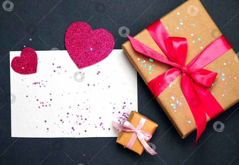 Скачать Фотография подарочной коробки с декором на день Святого Валентина, бумажное сердце, конфетти, лист бумаги на темно-сером фоне с видом сверху. фотосток Ozero