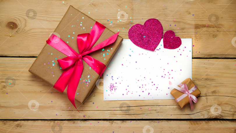 Скачать Фотография подарочной коробки с декором на день Святого Валентина, бумажное сердце, блестки и лист бумаги на деревянном фоне с видом сверху. фотосток Ozero