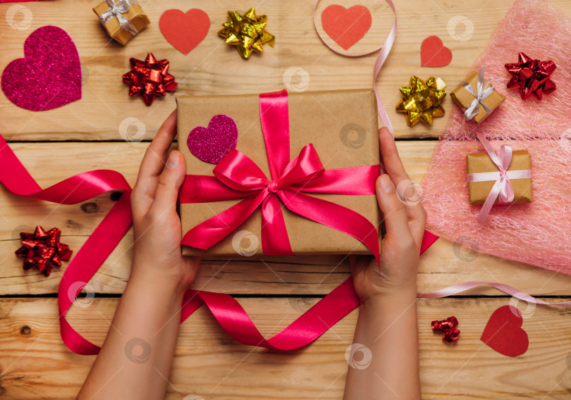 Скачать Женские руки держат подарочную коробку с розовой лентой на деревянном фоне. Концепция Дня святого Валентина, Дня матери. фотосток Ozero