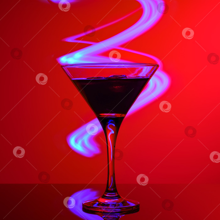 Скачать Красный тропический коктейль со льдом в бокале для мартини на фоне ярко-синих неоновых огней вечеринки в баре. фотосток Ozero