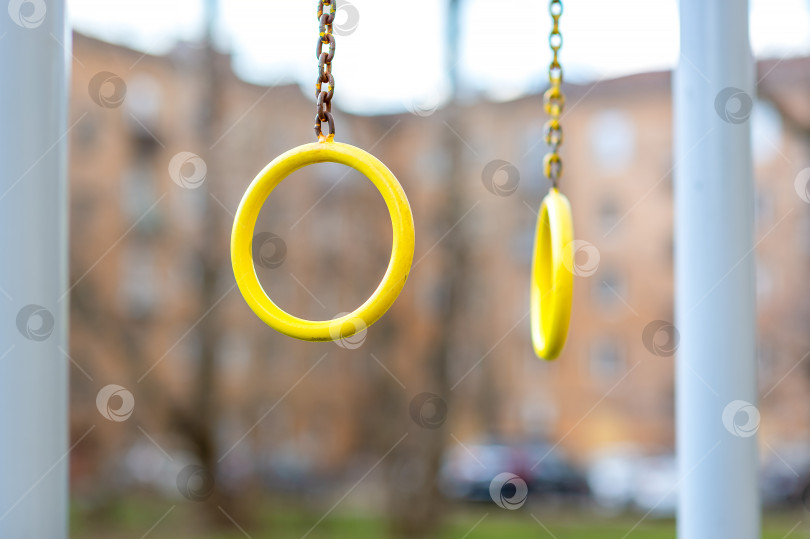 Скачать Желтое гимнастическое спортивное кольцо с железной цепью в центре внимания на открытой игровой площадке в городском дворе. фотосток Ozero