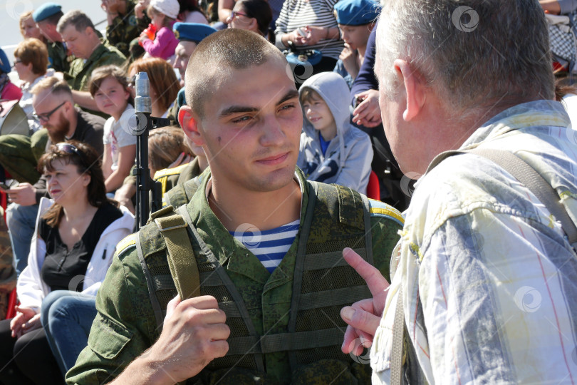 Скачать Десантник в тельняшке, в полевой одежде и с автоматом за спиной выслушивает наставления от ветерана ВДВ. Действие происходит 2 августа во время празнования дня ВДВ. Сзади видны зрители на стадионе. На некоторых одеты голубые береты. фотосток Ozero