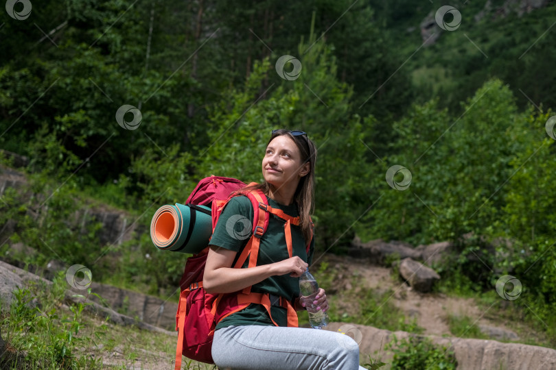 Скачать Женщина с рюкзаком сидит на скале и наслаждается живописным видом. Туристический поход и восхождение на горную вершину. Отдых во время горного похода фотосток Ozero