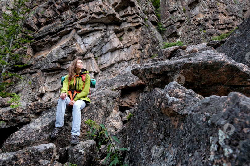 Скачать Женщина с рюкзаком сидит на скале и наслаждается живописным видом. Туристический поход и восхождение на горную вершину. Отдых во время горного похода фотосток Ozero