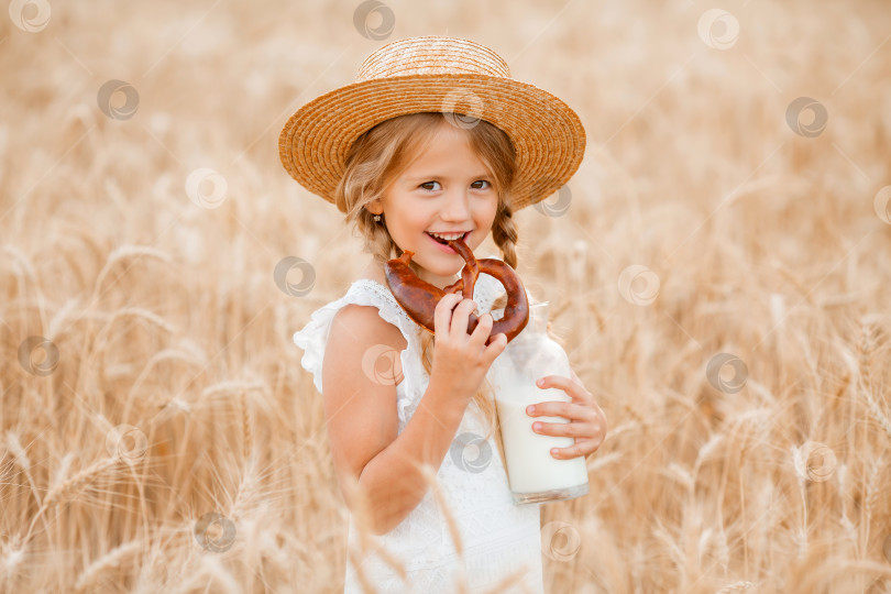 Скачать Маленькая белокурая девочка на пшеничном поле ест хлеб и пьет молоко. экологически чистые фермерские продукты фотосток Ozero