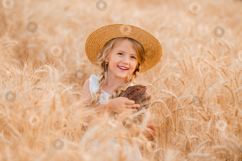Скачать Маленькая светловолосая девочка держит в руках свежую буханку хлеба на пшеничном поле летом. Экологически чистые фермерские продукты фотосток Ozero