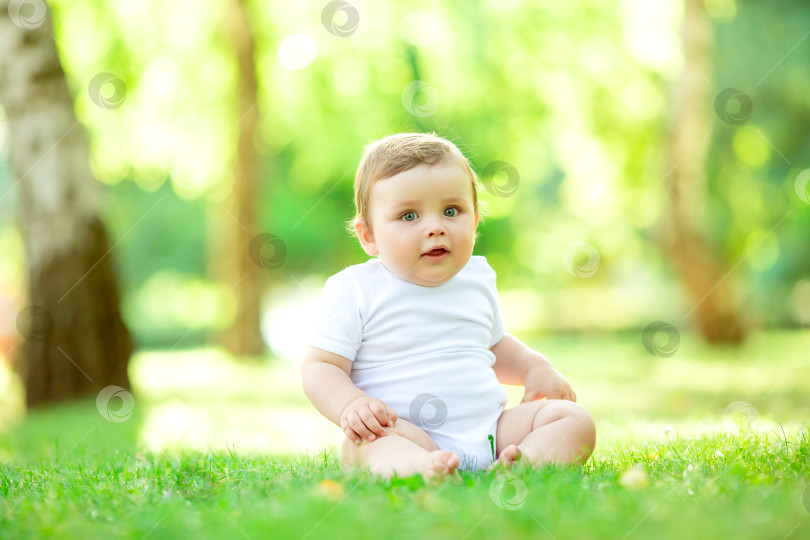 Скачать Симпатичный малыш 10 месяцев в белом боди сидит на зеленой летней траве, место для текста фотосток Ozero