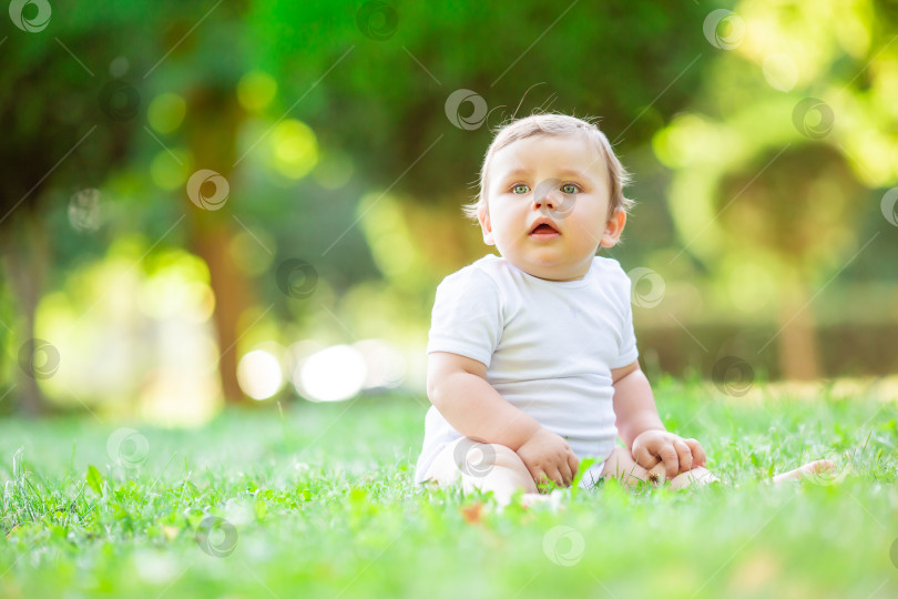 Скачать Симпатичный малыш 10 месяцев в белом боди сидит на зеленой летней траве, место для текста фотосток Ozero
