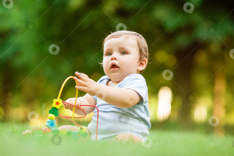 Скачать Здоровый малыш играет с развивающей игрушкой, сидя на летней траве фотосток Ozero