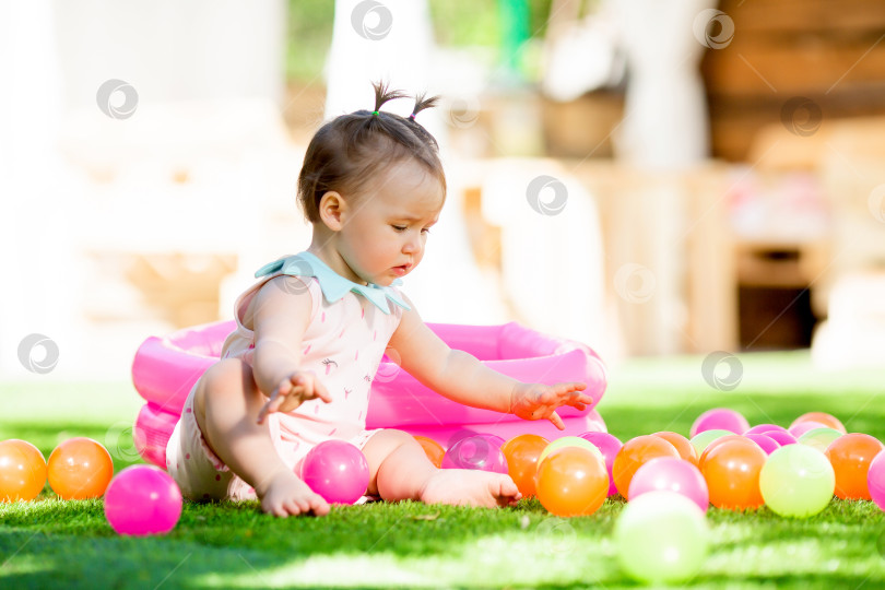 Скачать Маленькая девочка летом играет с развивающими игрушками на зеленой лужайке.Маленькая девочка играет в сухом бассейне фотосток Ozero