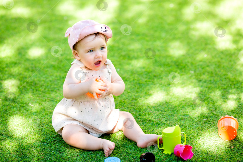 Скачать Маленькая девочка сидит летом на зеленой лужайке и играет в пирамиду фотосток Ozero