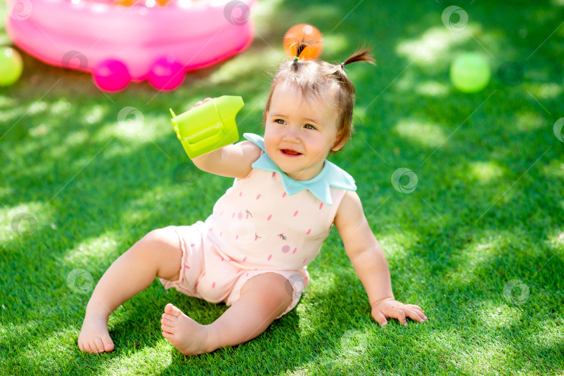 Скачать Маленькая девочка пьет воду из пластиковой бутылки, сидя летом на траве фотосток Ozero