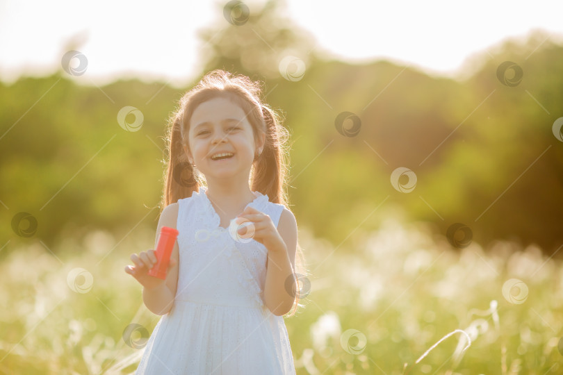 Скачать Маленькая девочка надувает мыльные пузыри летом на прогулке фотосток Ozero