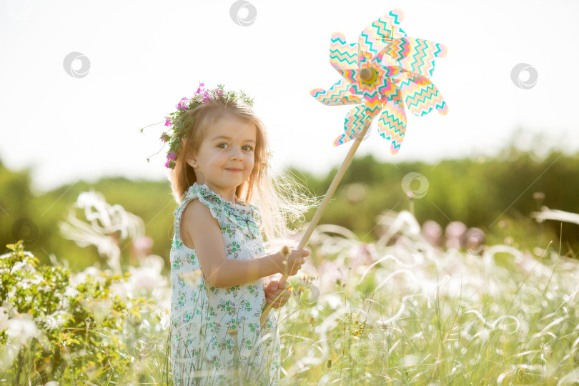 Скачать Милая маленькая девочка улыбается летом в поле, держа в руках ветряную мельницу фотосток Ozero