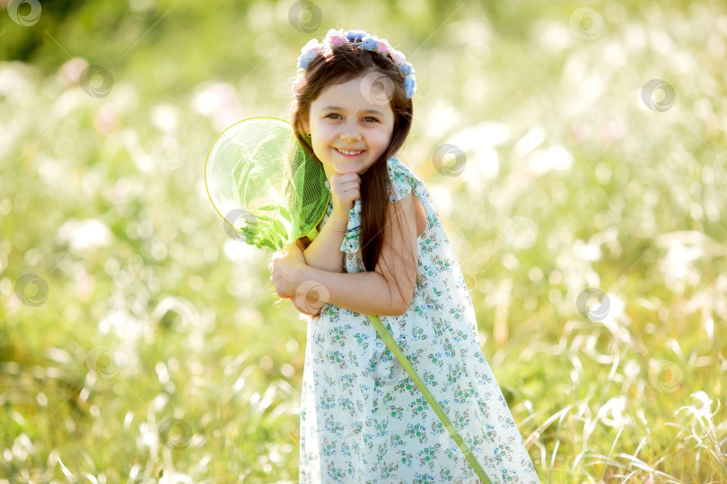 Скачать Милая маленькая девочка с венком на голове гуляет по полю и ловит сачком бабочек фотосток Ozero