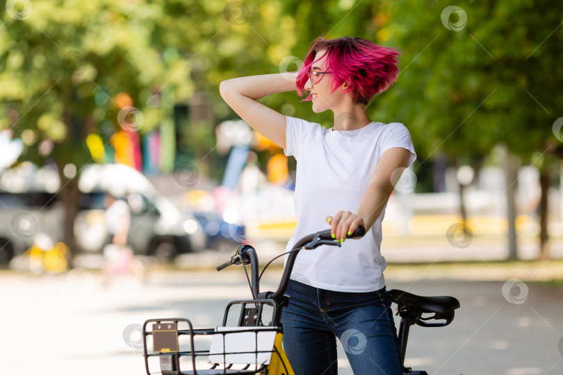 Скачать молодая женщина с розовыми волосами гуляет летом по парку на велосипеде и ест мороженое. Экологический вид транспорта фотосток Ozero