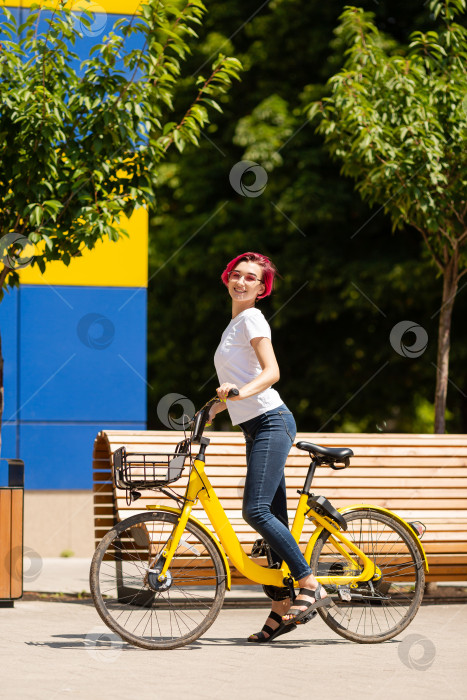 Скачать Счастливая молодая женщина с розовыми волосами летом прогуливается по городу на велосипеде. Экологичный вид транспорта фотосток Ozero