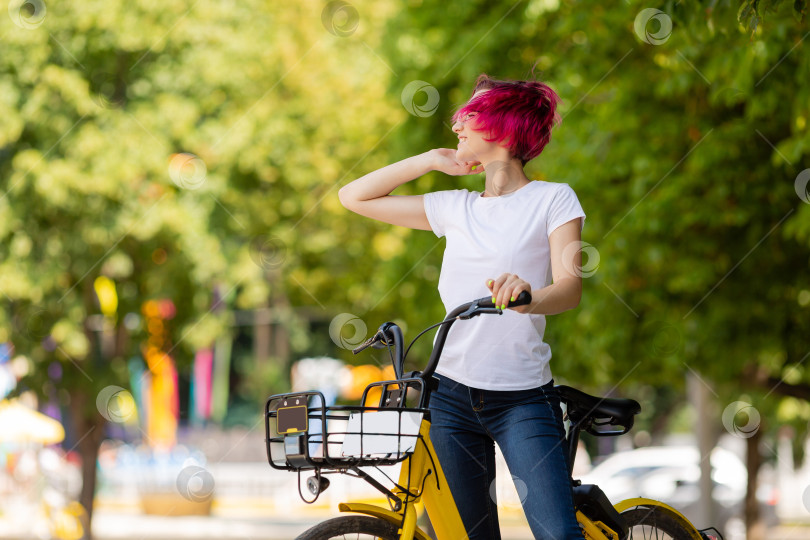 Скачать молодая женщина с розовыми волосами гуляет летом по парку на велосипеде и ест мороженое. Экологический вид транспорта фотосток Ozero