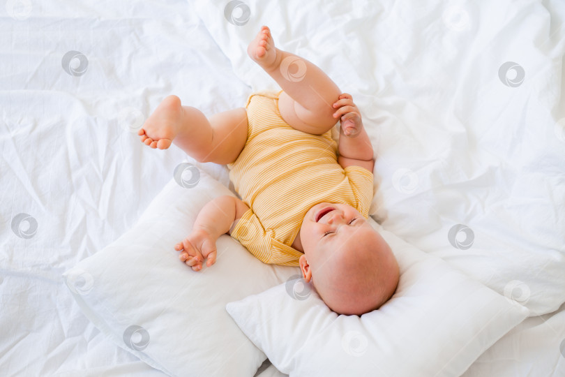Скачать Милый маленький мальчик, улыбаясь, лежит в кровати дома. постельное белье для детей фотосток Ozero