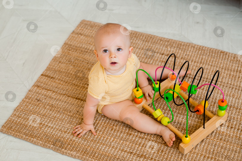Скачать Симпатичный малыш в желтом боди сидит дома на полу и играет в развивающую игрушку. концепция развития ребенка фотосток Ozero
