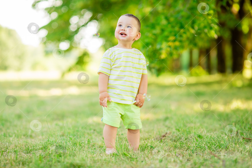 Скачать Счастливый годовалый мальчик летом играет с мыльными пузырями на открытом воздухе. Детский стиль фотосток Ozero