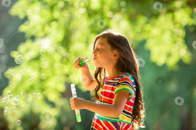 Скачать Счастливая маленькая брюнетка играет с летними мыльными пузырями в парке. Образ жизни детей фотосток Ozero