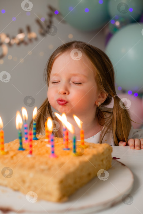 Скачать милая маленькая девочка задувает свечи на праздничном торте дома на фоне воздушных шаров. День рождения ребенка фотосток Ozero
