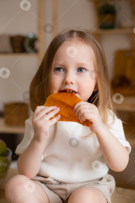 Скачать милая маленькая девочка ест натуральную пастилу дома на деревянной кухне. Питание для детей из натуральных продуктов фотосток Ozero