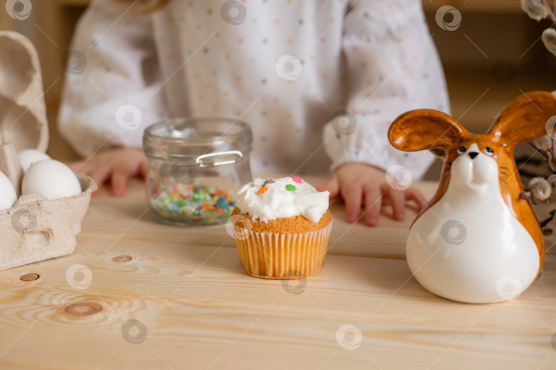 Скачать Милая маленькая девочка в хлопчатобумажном платье дома на деревянной кухне готовит пасхальный кулич фотосток Ozero
