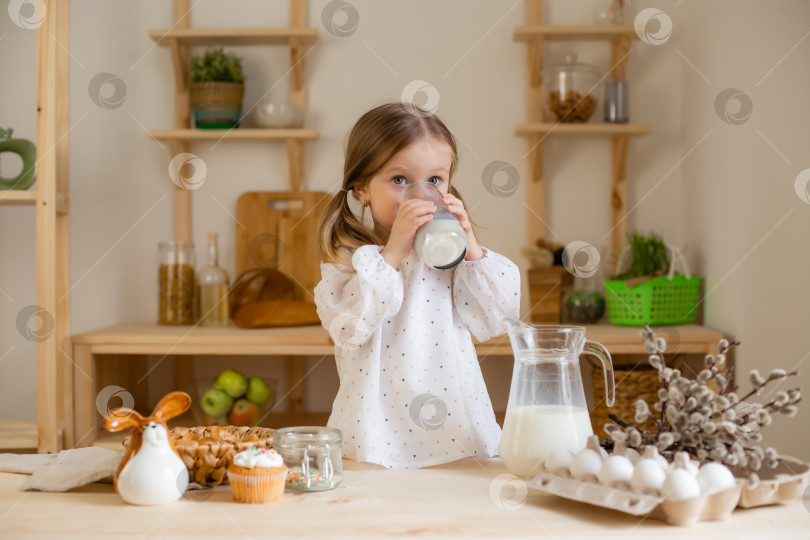 Скачать Милая маленькая девочка пьет молоко дома на деревянной кухне. Молочный день фотосток Ozero