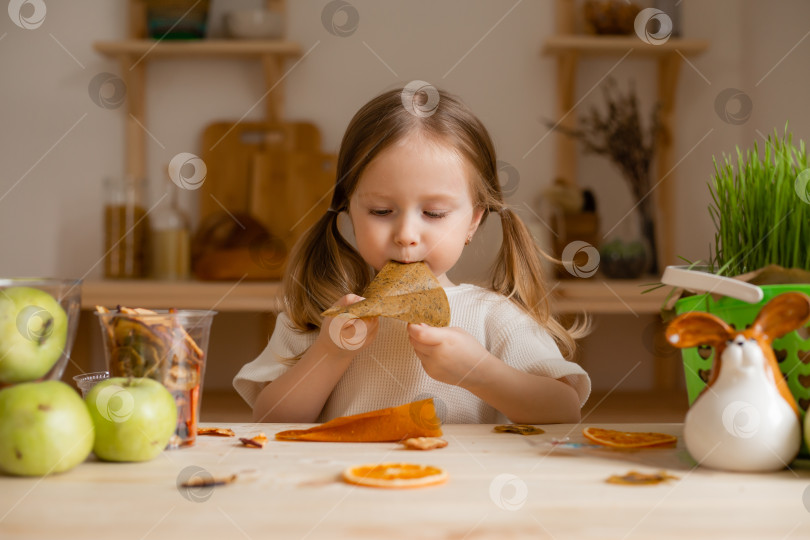 Скачать милая маленькая девочка ест натуральную пастилу дома на деревянной кухне. Питание для детей из натуральных продуктов фотосток Ozero