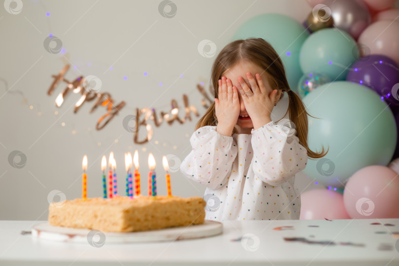 Скачать милая маленькая девочка задувает свечи на праздничном торте дома на фоне воздушных шаров. День рождения ребенка фотосток Ozero
