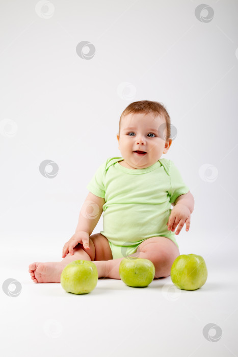 Скачать Симпатичный малыш в зеленом боди сидит с зелеными яблоками на белом фоне фотосток Ozero