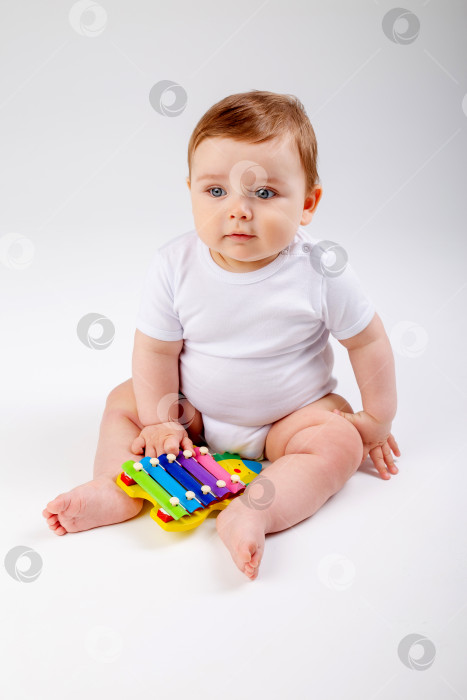 Скачать Симпатичный мальчик-карапуз 8 месяцев от роду в белом боди играет с развивающей игрушкой, сидящей на белом фоне, место для текста фотосток Ozero