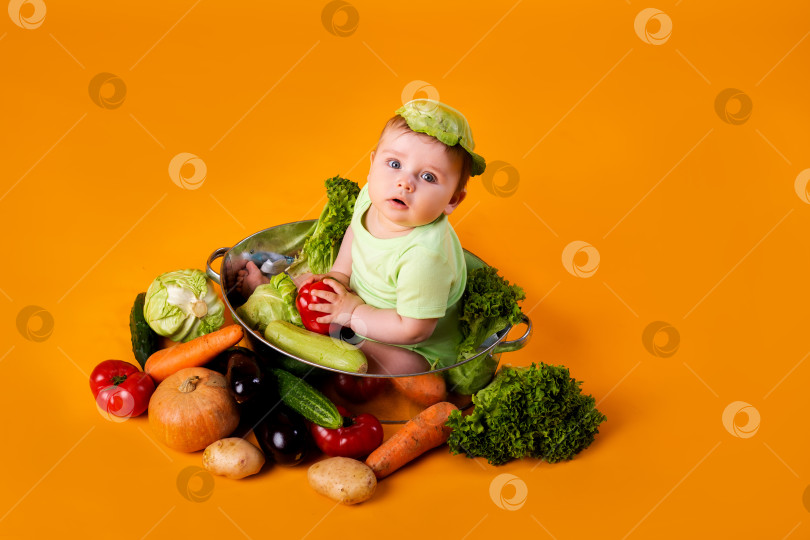 Скачать маленький мальчик в зеленом боди сидит в металлической миске с овощами на желтом фоне. концепция фермерского продукта, место для текста фотосток Ozero