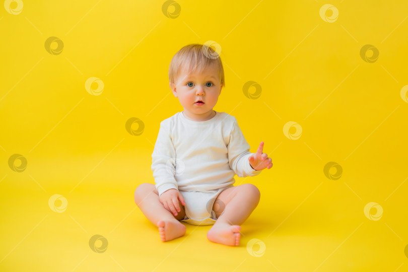 Скачать Здоровый ребенок в белом боди сидит на желтом фоне, место для текста фотосток Ozero