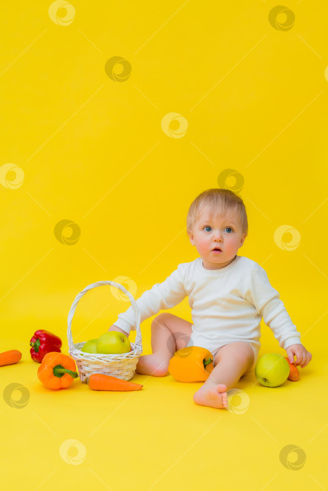 Скачать малышка в белом боди с овощами, сидящая на желтом фоне. здоровое питание для ребенка, место для текста фотосток Ozero