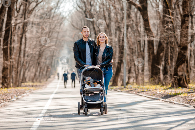 Скачать молодая семья прогуливается весной по парку с малышом в коляске. Счастливые родители фотосток Ozero