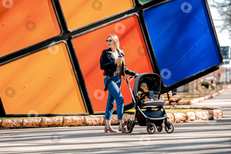 Скачать Молодая красивая мама гуляет по парку с малышом в коляске, пьет кофе фотосток Ozero